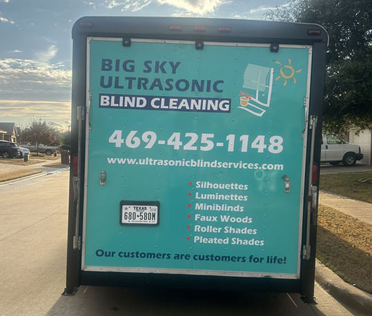 The back of a bright teal trailer advertising "Big Sky Ultrasonic Blind Cleaning," with contact info, services, and a customer-friendly message.