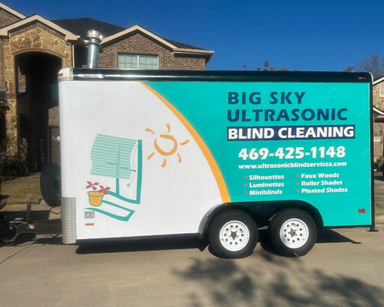 A trailer for Big Sky Ultrasonic Blind Cleaning, featuring vibrant graphics, contact info, and services offered, parked outside a home.