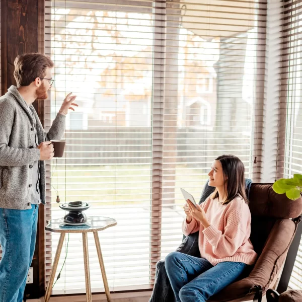A young couple happily talking with window blinds beside them.
