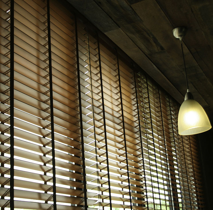 Light-filtering wooden blinds cover a window, with a soft hanging light bulb casting a warm glow in the room.